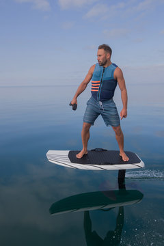 Man riding an electric hydrofoil foil board on a lake with a life jacket