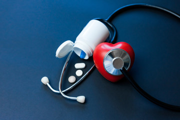 Red toy heart and stethoscope laying on dark background