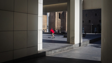 Un chico joven de jersey rojo practicando con su patinete en las calles de Barcelona