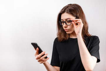 Fototapeta premium beautiful young woman on a white background looks at the phone with glasses and a black shirt. copyspace.
