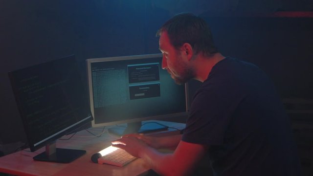 Cyber terrorist is hacking security system at night. Man is set on its work seriously. Male hacker smiles and shows the symbol fuck in the monitor display. cyber attack, internet, concept.