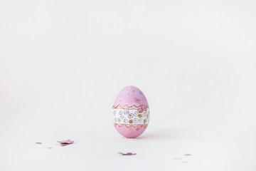 The pink Easter egg stands on a white background. Hand-painted patterns on an egg. Lonely holiday egg stands on the table