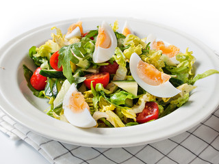 Fresh vegetable salad with mustard dressing and boiled eggs in a white plate (diagonal view, white background)