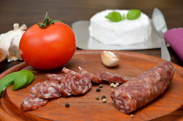 sausage with pepper and vegetables on a wooden board and cheese in the background