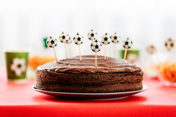 Simple chocolate cake with chocolate frosting and cake candles shaped as soccer balls. Football theme for kids birthday party.