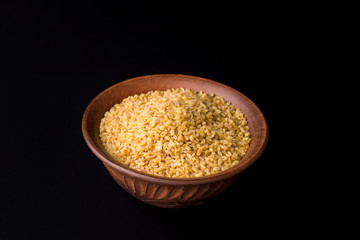 Raw bulgur groats on a black background in a traditional bowl