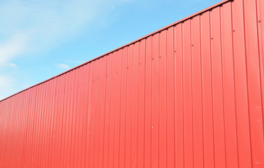 Fototapeta na wymiar Metal fence design: a red corrugated steel fence panels agains blue sky.