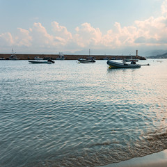 a fragment of a sandy beach with a moving sea wave with small motor boats parked in a quiet bay in the Greek resort of Hersonissos