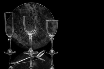 Verres à pied et assiette sur fond noir avec reflet.	