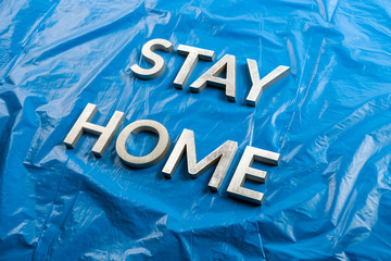 the words stay home laid with silver metal letters on crumpled blue plastic background in slanted...