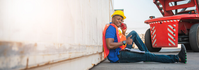 Fototapeta premium Black foreman worker working control the crane and forklift at Container cargo harbor to loading containers. African dock male staff with radio for Logistics import export shipping concept.