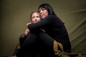 Mother and daughter in black clothes hug sitting on a green background. A woman and a child are...