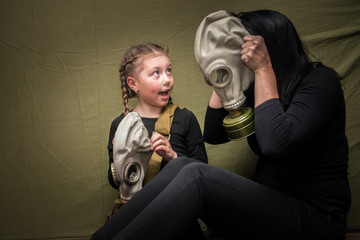 A woman shows a girl how to use a gas mask correctly. Mom teaches her daughter to put a gas mask on her head. The family in the shelter learn to use protective equipment.
