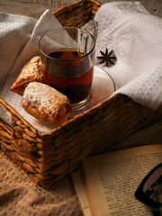 Tea and sweet cookies in a wicker tray on white wooden background. Open Book near the afteroon tea