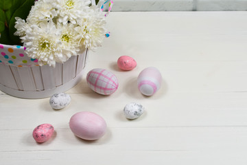 Easter concept. Easter pink eggs near a basket with white flowers on a wooden table on a background of a white wall. Place for an inscription. For postcards.