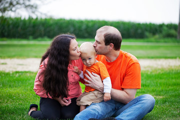 Naklejka na ściany i meble Portrait of happy parents kissing their baby son outdoors