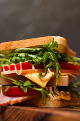 Huge delicious sandwich with ham and sturgeon, arugula, cheese, tomato and mayonnaise on a cutting board in a rustic style on the gray background a side view, close-up