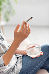 cropped view of of mature woman holding rolled joint with legal marijuana and ashtray