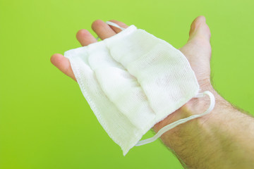 hand holds surgical mask, medical protective mask isolated on green background. Covid-19 virus protection concept