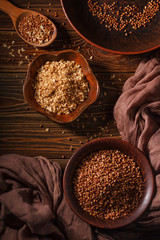 Rural still life with top view of the buckwheat flakes and the peeled groats of buckwheat, on a wooden surface closeup