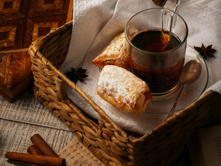 Tea with sweet cookies in a wicker tray on white wooden background. Cinnamon stiks lay near the afteroon tea