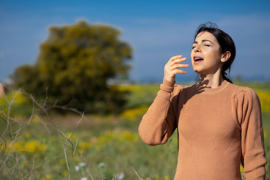 Donna con maglione color cachi starnutisce  e si protegge con la mano, sfondo natura