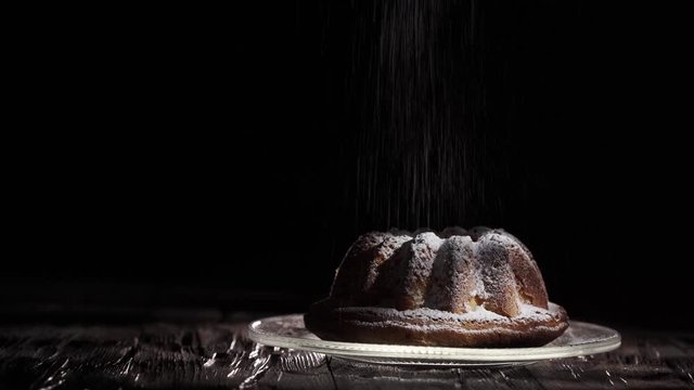 Babka - Ciasto na stole ( deska ) . Ciemne tło . Cukier puder .  Posypywanie cukrem pudrem. 