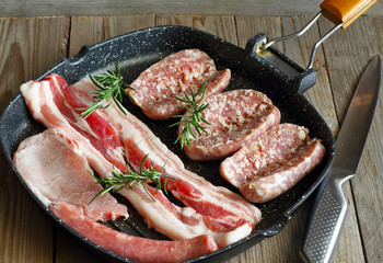 Carne di maiale cruda. Salsiccia pancetta braciola con rosmarino su piastra antiaderente pronta per la cottura sul fuoco.