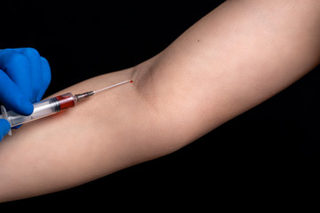 doctor in disposable gloves holds a syringe with a vaccine near the patient's vein