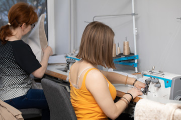 Two women - a teenager and an experienced dressmaker sew protective masks on the overlock.