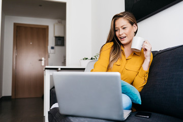 Pretty long haired female sitting on sofa with portable computer working remotely from home.