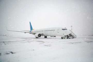 Passenger plane at airport in winter in blizzard. Landing passengers in airliner in winter during...