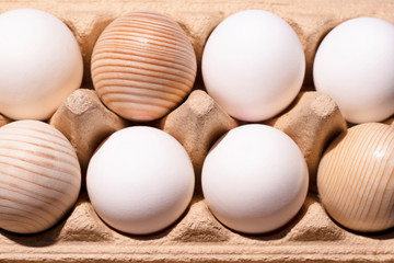 White and wooden eggs lie in two rows in paper packaging. The eggs were shot close-up and flat lay. There is a shadow. Minimalistic and high-quality photo for your design.
