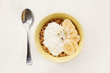 Muesli, granola with yogurt and banana in yellow bowl, spoon on white background. Top view