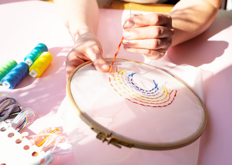 Hands of female sewing rainbow small embroidery pattern in wooden frame, colourful threads on...