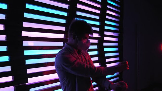 Cool handsome guy in protective medicine mask enjoying favorite track dancing in neon nightclub. Portrait of excited young man moving into music. colorful lights disco rave party. Pandemic leisure