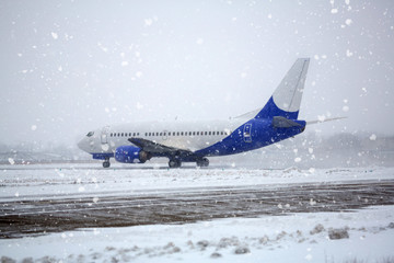 Airliner on runway in blizzard. Aircraft during taxiing on landing strip during heavy snow....
