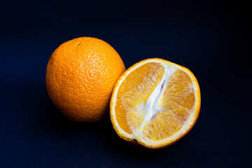 One whole orange and a half of an orange arranged on dark black background, side view