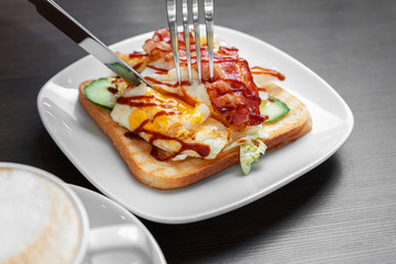 An egg and bacon sandwich is cut with a knife and fork.