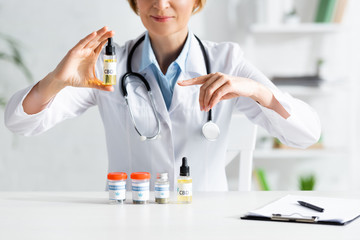 cropped view of doctor in white coat pointing with finger at bottle with cbd lettering
