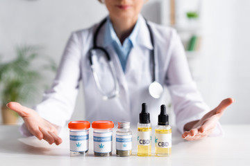 cropped view of doctor pointing with hands at bottles with cbd and medical cannabis lettering