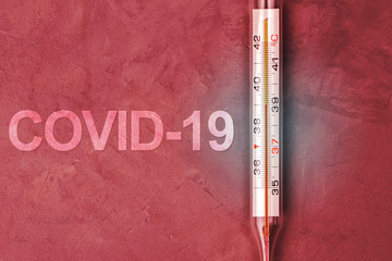 Thermometer with 39 degrees on a dark red background near the inscription COVID-19.