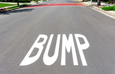 BUMP traffic warning sign painted on residential street surface. Background, speed bump painted brown for better visibility.