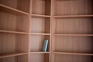 A single book sitting on an empty bookshelf