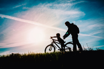 father help little daughter to ride bike at sunset nature