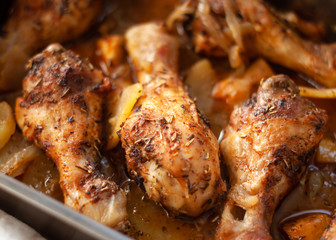 Roasted Chicken legs on metal baking tray with potatoes, onion. tomatoes witn spices. Top view.