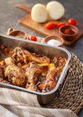Roasted Chicken legs on metal baking tray with potatoes, onion. tomatoes witn spices.