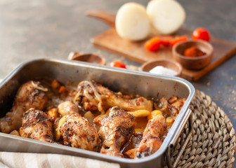 Roasted Chicken legs on metal baking tray with potatoes, onion. tomatoes witn spices. Closeup with copy space.