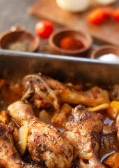 Freshly and spicy cooked drumstick on a oven tray witn potatoes and onion and some tomatoes. Close up.
