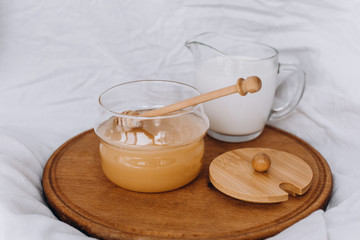 Fototapeta na wymiar Honey and milk in a glass bowl on a wooden stand. White fabric background